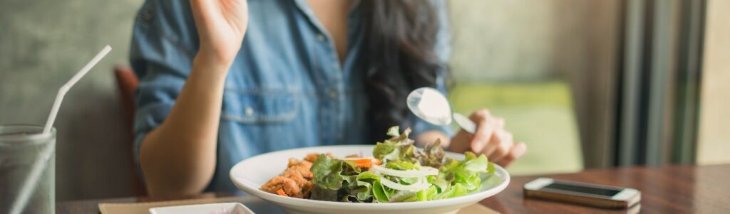 imagen de un plato de verduras con una mujer en la parte de a tras comiendo del plato
